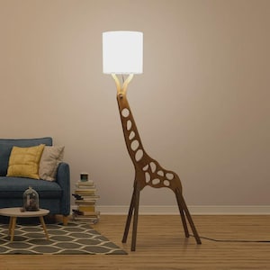 May include: A unique floor lamp shaped like a giraffe. The lamp is made of wood with a light brown finish and features a white lampshade. The giraffe's body has cut-out spots. The lamp is plugged into an electrical outlet.