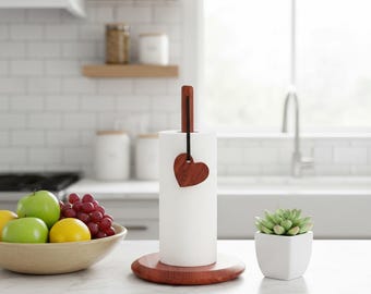 Peut inclure: Un porte-serviettes en papier blanc avec une base et une poignée en bois. Un cœur en bois orne le dessus. Un bol de fruits et une petite plante succulente en pot suggèrent une ambiance de cuisine.