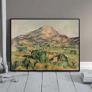 May include: A framed landscape painting featuring a mountain and valley scene. The artwork uses a palette of greens, yellows, and browns to depict trees, fields, and buildings. The mountain dominates the background, with a soft, muted sky.