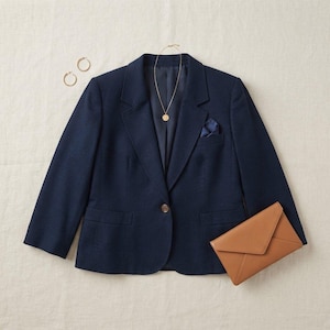 Puede incluir: Un blazer azul marino con cierre de un solo botón, dos bolsillos con solapa y solapa de muesca. El blazer se combina con un collar de cadena dorada, dos pendientes de aro dorados, un pañuelo de bolsillo azul oscuro y un bolso de mano beige.