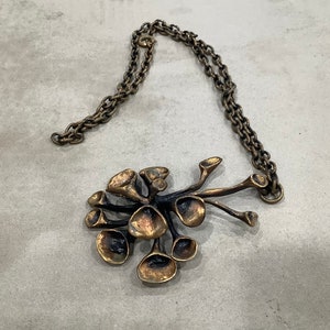 May include: A bronze necklace with a pendant shaped like a cluster of stylized flowers. The pendant is made of multiple interconnected pieces, each with a unique shape and texture.