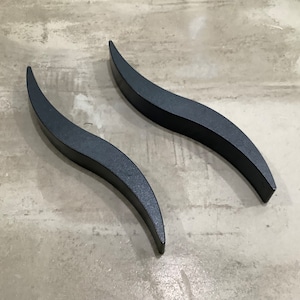 Puede incluir: Dos tiradores de metal negro con un diseño ondulado. Los tiradores son lisos y tienen un acabado mate.