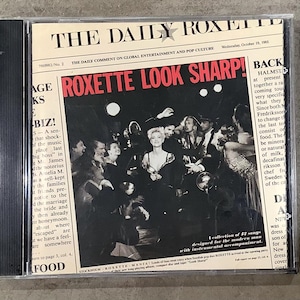 May include: CD case for the Roxette album "Look Sharp!" featuring a black and white image of a group of people. The album cover resembles a newspaper with the band's name in large red letters.