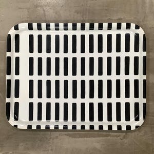 May include: Rectangular serving tray with a white background and a repeating pattern of vertical black rectangles. The tray has rounded corners and a glossy finish, suitable for serving food or displaying items.