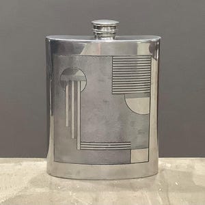 May include: A silver-colored flask with a geometric design etched on the front. The design includes a circle, rectangles, and lines. The flask has a small, screw-on cap at the top.