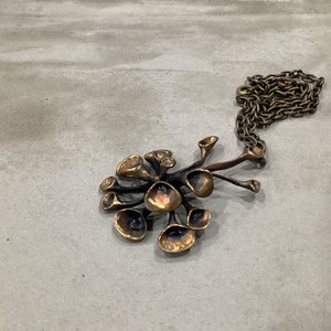 May include: A bronze pendant necklace with a cluster of abstract, organic shapes resembling flowers or mushrooms. The pendant is attached to a chain.