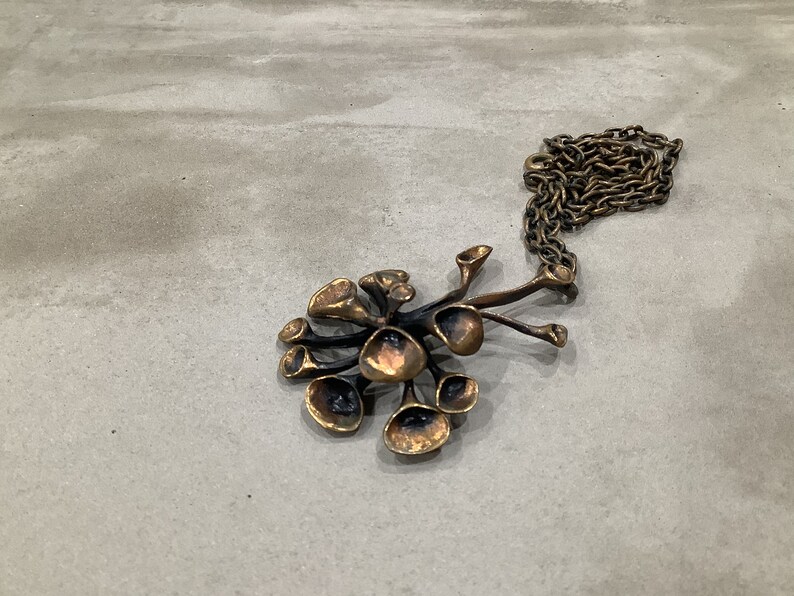 May include: A bronze pendant necklace with a cluster of abstract, organic shapes resembling flowers or mushrooms. The pendant is attached to a chain.
