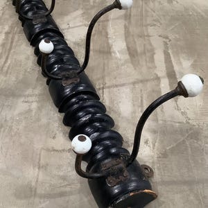 Puede incluir: Un perchero de madera negro con un diseño en espiral. Cuenta con varios ganchos de metal curvados con pomos de cerámica blanca. El perchero está montado en una pared y tiene una estética rústica y vintage.