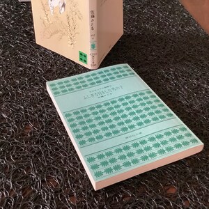 May include: A light blue book with a green and white pattern on the cover. The title of the book is "ひっそりと咲く花" which translates to "Quietly Blooming Flowers".