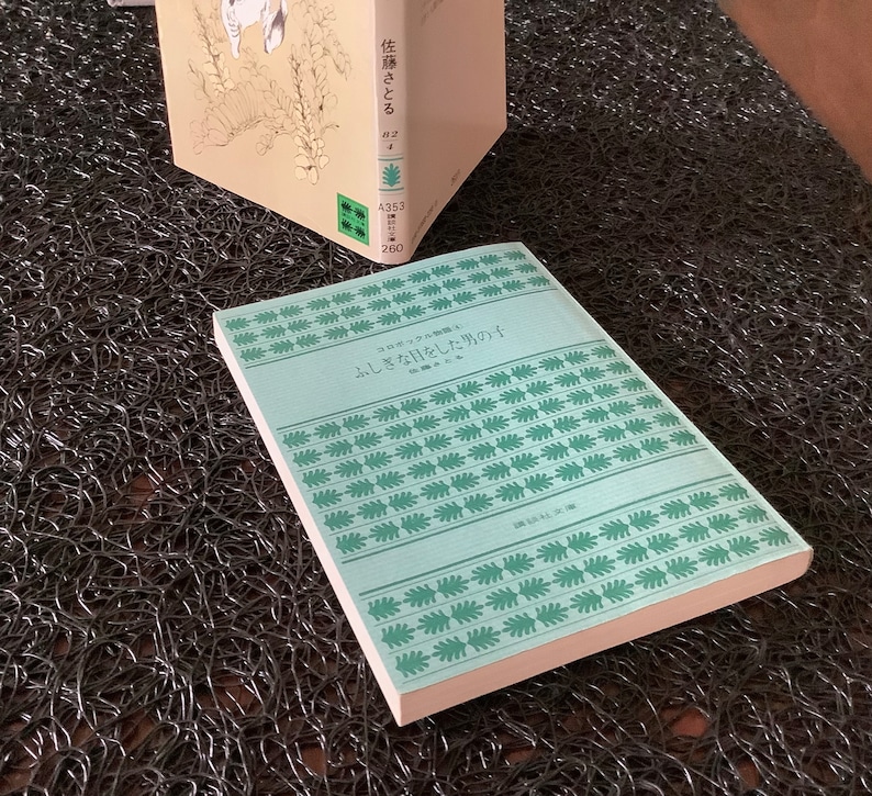 May include: A light blue book with a green and white pattern on the cover. The title of the book is "ひっそりと咲く花" which translates to "Quietly Blooming Flowers".