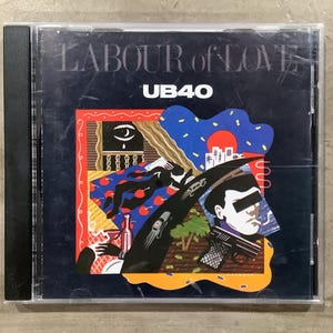 Puede incluir: Una caja de CD con el título del álbum "LABOUR of LOVE" y el nombre del artista "UB40" impresos. La obra de arte presenta un collage de ilustraciones en rojo, azul y negro, incluyendo un ojo, figuras y un paisaje urbano.