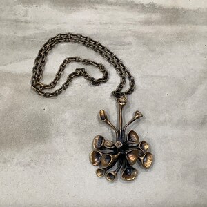 May include: A bronze necklace with a pendant shaped like a stylized flower with multiple petals. The pendant is attached to a chain.