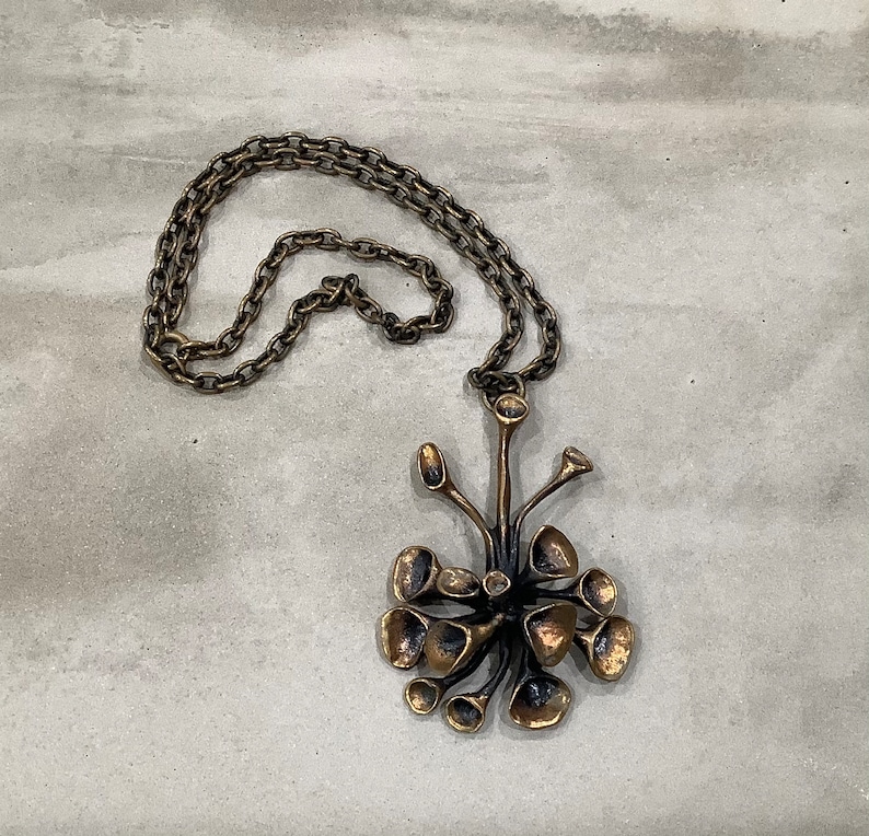 May include: A bronze necklace with a pendant shaped like a stylized flower with multiple petals. The pendant is attached to a chain.