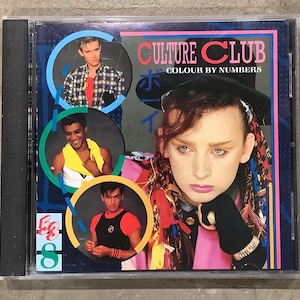 May include: A CD case featuring the album "Colour by Numbers" by Culture Club. The cover art includes portraits of the band members in circular frames, with Boy George in the foreground. The album title is in pink and red, with Japanese text.