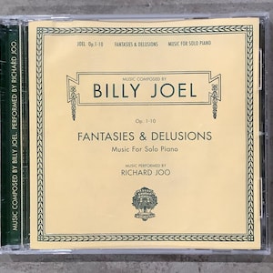 May include: A CD case featuring the album "Fantasies & Delusions" by Billy Joel, performed by Richard Joo. The cover has a cream-colored background with green and black text. The text includes the album title, composer, and performer.