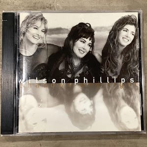 May include: A CD case featuring a black and white image of three women smiling. The text "wilson phillips" is visible on the cover. The image is a close-up shot of the CD case.