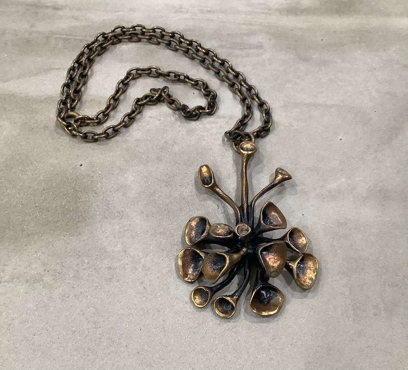May include: A bronze necklace with a pendant shaped like a stylized flower with multiple petals. The chain is made of linked circles.