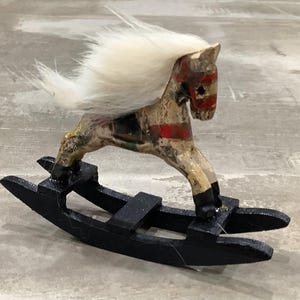 May include: A white rocking horse with a black base and a white fur mane and tail. The horse is painted with red, white, and blue stripes.
