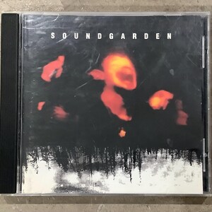 May include: A Soundgarden CD case with a black spine. The album cover features the band's name in white letters at the top. The artwork shows blurred red and orange figures against a dark background, with a white and gray forest scene at the bottom.