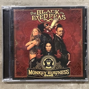 May include: A CD case featuring the album "Monkey Business" by The Black Eyed Peas. The cover art showcases the band members against a red backdrop with ornate designs. The album title and band name are prominently displayed.