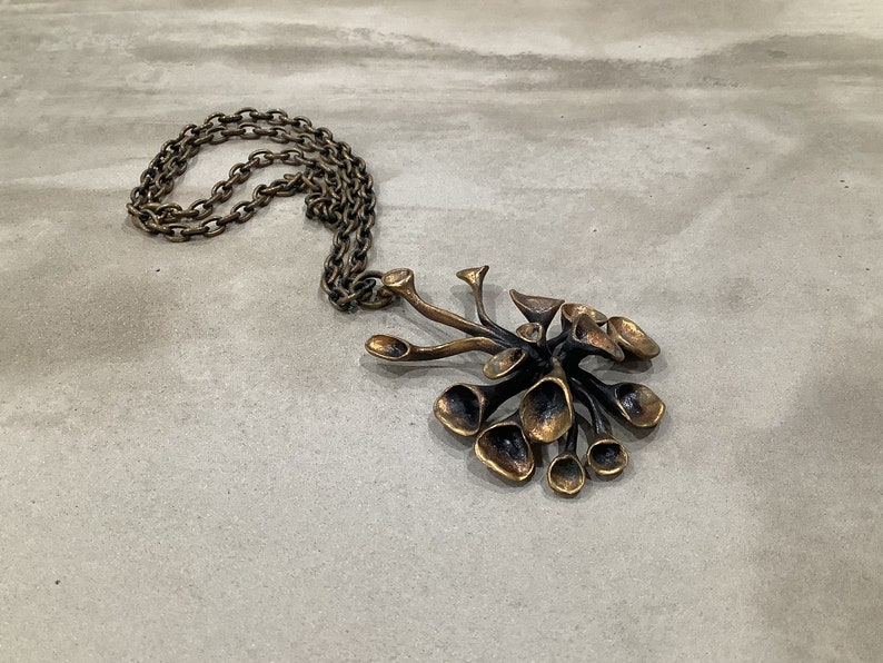 May include: A gold-toned necklace with a large, abstract pendant. The pendant is made of multiple, interconnected, organic shapes that resemble a flower or a cluster of leaves.
