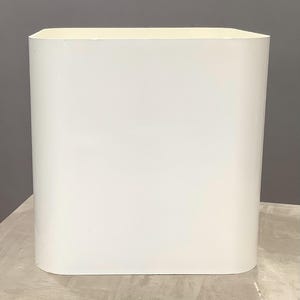 May include: A white, rectangular, modern-style planter with rounded corners. The planter has a smooth, matte finish and a slightly off-white color. The planter is empty and sits on a light-colored surface.