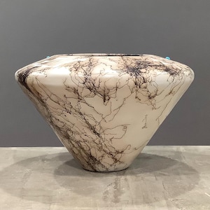 May include: A wide, conical ceramic vessel with a smooth, off-white glazed surface featuring intricate, dark brown, branching, vein-like patterns that wrap around the exterior. The rim is circular with small, bright turquoise accents.