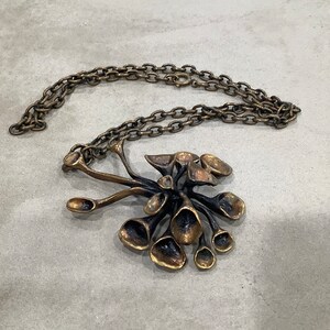 May include: A gold-toned necklace with a large, abstract pendant. The pendant is made of multiple interconnected, organic shapes that resemble flowers or leaves.