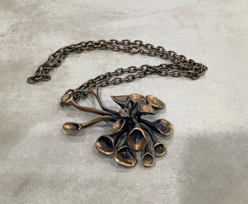 May include: A gold-toned necklace with a large, abstract pendant. The pendant is made of multiple interconnected, organic shapes that resemble flowers or leaves.