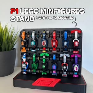 Op de afbeelding: Een zwarte displaystandaard met twaalf kleurrijke F1 Lego raceauto's. De standaard heeft een rode basis en de tekst "F1 LEGO MINIFIGURES STAND FOR THE 12 MODELS". De auto's zijn in verschillende kleuren.