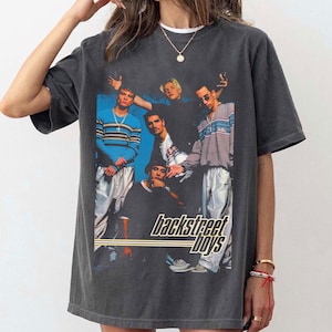 May include: Dark gray t-shirt featuring a group photo of the Backstreet Boys. The image shows the band members in various outfits, with the band's name in a stylized font at the bottom. The shirt has a vintage, worn look.