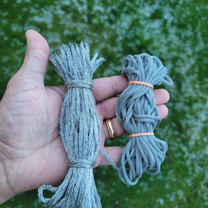 May include: Two bundles of grey cordage. The left bundle is a textured, fibrous grey cord tied at both ends. The right bundle is a smooth, solid grey cord secured in the centre and at the top with thin, bright orange rubber bands.