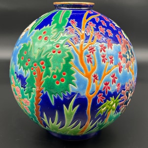 May include: A spherical ceramic vase with a detailed landscape design. The vase has a blue background with green trees, red berries, and orange tree trunks. The rim has a gold trim.