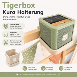 Könnte beinhalten: Ein hellgrüner, quadratischer Halter für eine Tigerbox, der auf der Vorderseite ein kleines Katzengesicht auf dem Gitter zeigt. Der Halter ist zur Befestigung an einem Holzrahmen konzipiert und enthält deutschen Text zu den Produktmerkmalen.