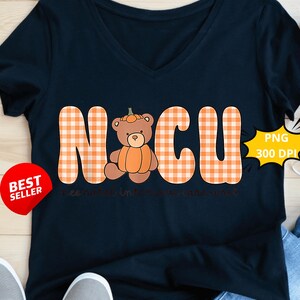 Peut inclure: T-shirt bleu marine à col en V avec les lettres "NICU" en motif à carreaux orange et blanc. Un ours en peluche marron portant un costume de citrouille orange est au centre. Les mots "Neonatal Intensive Care Unit" sont en dessous.