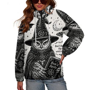 May include: A white quarter-zip pullover featuring a black and white graphic print of an owl wearing a witch hat and holding a Book of Spells. The design includes pentagram symbols, a crescent moon, and text that reads Don't make me flip my witch switch.