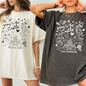 May include: Two oversized t-shirts, one cream and one charcoal, featuring a whimsical black and white graphic. The design includes a castle, Mickey Mouse ears, and the text "going to the Castle". One shirt says "Future Mrs. Smith", the other says "Amy's Bachelorette".