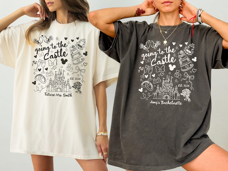 May include: Two oversized t-shirts, one cream and one charcoal, featuring a whimsical black and white graphic. The design includes a castle, Mickey Mouse ears, and the text "going to the Castle". One shirt says "Future Mrs. Smith", the other says "Amy's Bachelorette".