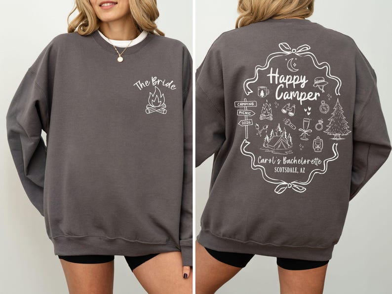 K&ouml;nnte beinhalten: Anthrazitfarbenes Sweatshirt mit wei&szlig;em Text und Grafiken. Auf der Vorderseite steht "The Bride" &uuml;ber einer Lagerfeuergrafik. Die R&uuml;ckseite zeigt ein "Happy Camper"-Design mit Camping-Symbolen und "Carol's Bachelorette Scottsdale, AZ".