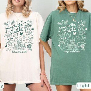 May include: Two t-shirts, one ivory and one light green, feature a whimsical design with the text "going to the Castle." The design includes a castle, Mickey Mouse ears, and wedding-themed illustrations. One shirt says "Future Mrs. Smith," the other says "Amy's Bachelorette."