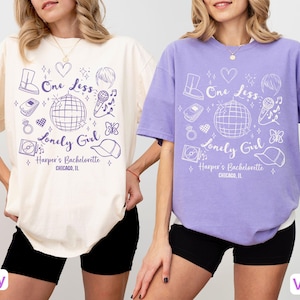 May include: Ivory and violet oversized t-shirts with a graphic design. The design includes the text "One Less Lonely Girl" and "Harper's Bachelorette CHICAGO, IL" along with illustrations of a disco ball, microphone, and other icons.