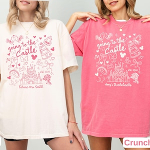 May include: Two t-shirts, one ivory and one crunchberry, with a pink graphic. The graphic includes the text "going to the Castle", a castle illustration, and other wedding-themed icons. The ivory shirt says "Future Mrs. Smith" and the crunchberry shirt says "Amy's Bachelorette".