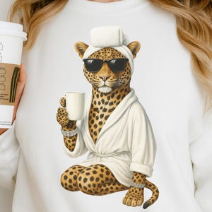 Pode incluir: Uma ilustração digital de um leopardo usando óculos de sol, um roupão branco e uma toalha na cabeça, segurando uma caneca branca. O leopardo está sentado com as pernas cruzadas. O leopardo tem uma pelagem manchada e está usando uma pulseira no pulso e no tornozelo.