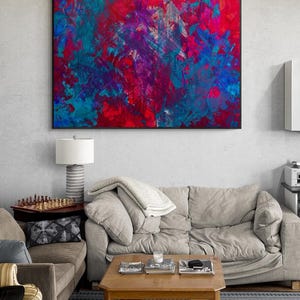 Può includere: Opera d'arte astratta con cornice nera, che presenta una miscela di tonalità rosse, blu e viola. Il dipinto è appeso sopra un divano beige in un soggiorno.
