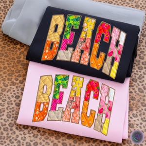 Puede incluir: Sudaderas negras y rosas con la palabra "BEACH" aplicada en telas coloridas estampadas. Las sudaderas están dobladas y apiladas, con una sudadera gris encima. El fondo tiene un estampado de leopardo.