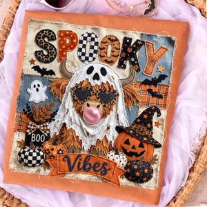 May include: A fabric wall hanging featuring a Highland cow wearing a ghost costume, heart-shaped sunglasses, and blowing a pink bubble. The text reads SPOOKY VIBES and BOO. The design includes pumpkins, bats, and stars in orange, black, and white.