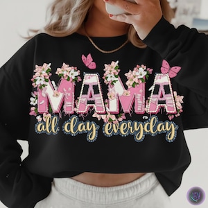 Könnte beinhalten: Schwarzes Sweatshirt mit dem Wort "MAMA" in rosa Buchstaben, verziert mit Blumen und Perlen. Der Satz "all day everyday" steht in goldener Schrift darunter. Rosa Schmetterlinge sind ebenfalls abgebildet.