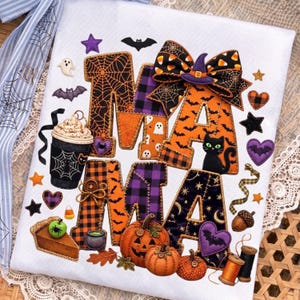 May include: A white fabric surface featuring the word MAMA in large, patterned letters decorated with Halloween motifs like spiderwebs, bats, and ghosts. The design includes a coffee cup, pumpkins, a pie slice, and a large bow with candy corn.