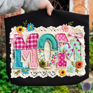 Puede incluir: Bolso tote negro con la palabra "MOM" aplicada en tela colorida. Las letras presentan varios patrones, incluyendo cuadros, lunares e estampados florales, con flores bordadas y un borde de encaje.