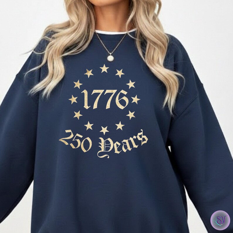 May include: Navy blue sweatshirt with a white crew neck collar. The front features the text "1776" surrounded by stars, with "250 Years" below in a decorative font. The design is in a gold color.